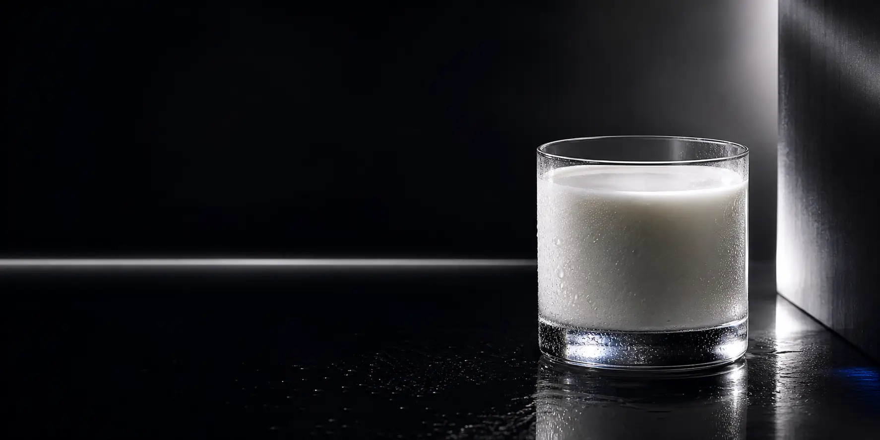 A cold glass of milk illuminated on a dark reflective surface.
